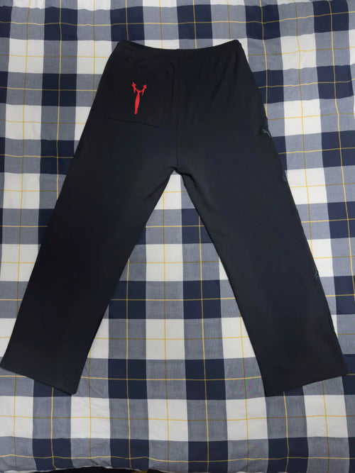Black athletic pants with a small red kangaroo pocket and logo on the left hip, laid flat on a blue, white, and yellow plaid blanket.